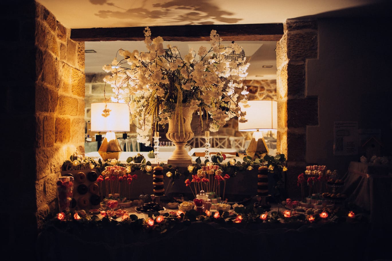 Mesa dulce decorada con flores blancas y luces cálidas entre paredes de piedra