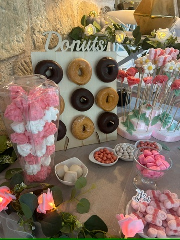 Mesa dulce con panel de donuts, chuches y decoración floral rosa